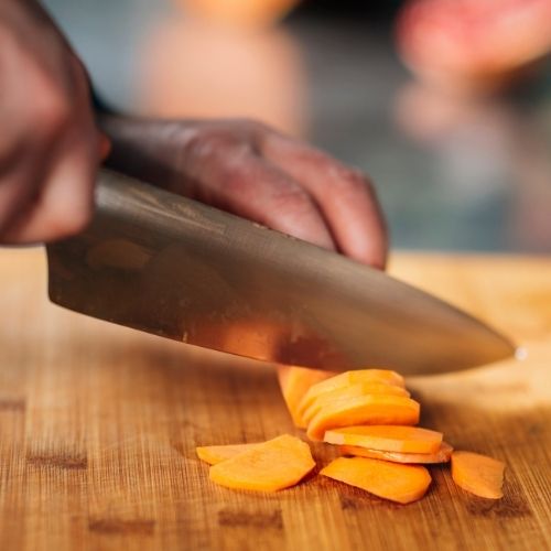 main qui coupe une carotte sur une planche avec un couteau 